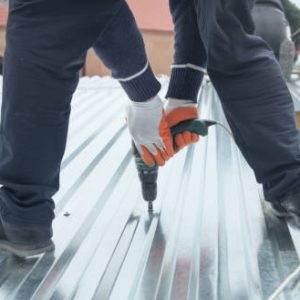 Man installing metal sheet roof by electrical drilling machine.